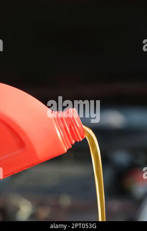 Versando olio motore dal contenitore rosso su sfondo sfocato, primo piano Foto Stock