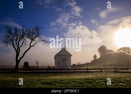 Sole di mattina presto, nebbia e nebbia sulla piccola chiesa rurale in campo Foto Stock