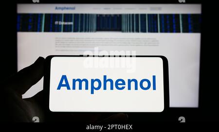 Persona che tiene il cellulare con il logo della società di elettronica americana Amphenol Corporation sullo schermo di fronte al sito web aziendale. Messa a fuoco sul display del telefono. Foto Stock