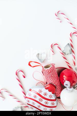 Le caramelle di Natale, insieme ai taglierini dei biscotti, ai giocattoli dell'albero di Natale ed al filo rosso per il rivestimento del regalo, si trovano su un tavolo bianco. Messa a fuoco selettiva, rumore. CHRI Foto Stock