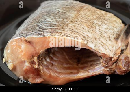 Un pezzo grezzo di carpa d'argento si trova su un piatto nero Foto Stock