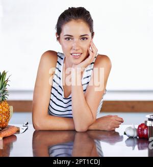 Im sicuro nelle mie scelte sane. Un ritratto di una bella giovane donna appoggiata sul suo bancone da cucina accanto al cibo e ad una pentola da cucina Foto Stock