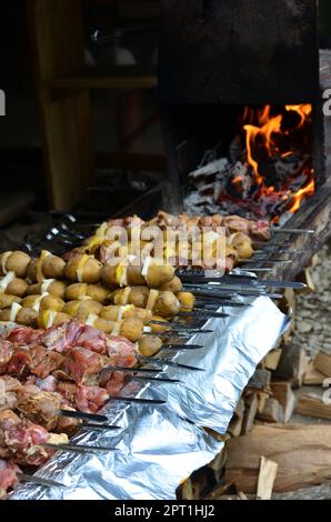 La carne cruda e le patate sono piantati su spiedini di metallo. Il processo di cottura shish kebab. Russo e ucraino cibo camp Foto Stock