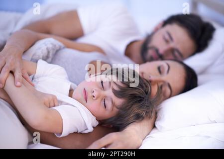 Vuole sempre essere vicino alla mamma e al papà. una giovane famiglia a letto insieme Foto Stock