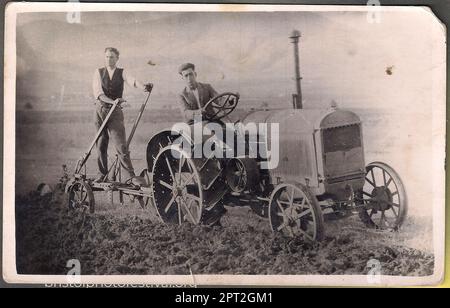 Due uomini che arano un campo con un trattore (1932?) Foto Stock