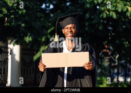 Ritratto di ragazzo nero sorridente in piedi con ulodato cartoncino vuoto poster sulla strada in cerca di lavoro, spazio copia libero. Università o università Foto Stock