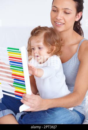 Imparare a casa. Una giovane madre che insegna alla bambina le basi della matematica usando un abaco Foto Stock