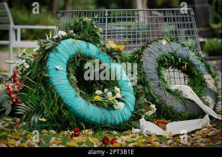 vecchie corone funebri accanto a un cestino di rifiuti in un cimitero Foto Stock