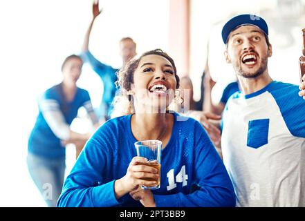 Theyre una partita fatta in paradiso sportivo. un giovane uomo e una donna che beve una birra mentre guardano una partita di sport in un bar. Foto Stock