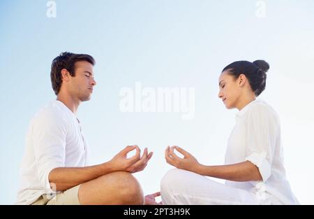 Trovare pace e tranquillità tra di loro. Una giovane coppia che esegue una rilassante routine di yoga insieme sulla spiaggia Foto Stock