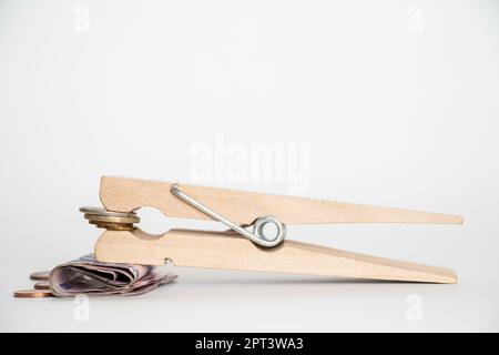 Un grande clothespin di legno tiene le monete ucraine e le hryvnie di carta su un fondo bianco, finanza Foto Stock