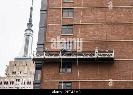 I lavoratori conducono mattoncini rimodelinando su una piattaforma sospesa con l'Empire state Building sullo sfondo, 2023, New York City, Stati Uniti Foto Stock