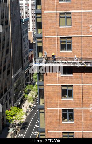 I lavoratori conducono un rimando di mattoni su una piattaforma sospesa in un edificio nel centro di Manhattan, 2023, New York City, Stati Uniti Foto Stock