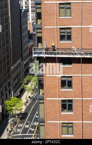 I lavoratori conducono un rimando di mattoni su una piattaforma sospesa in un edificio nel centro di Manhattan, 2023, New York City, Stati Uniti Foto Stock