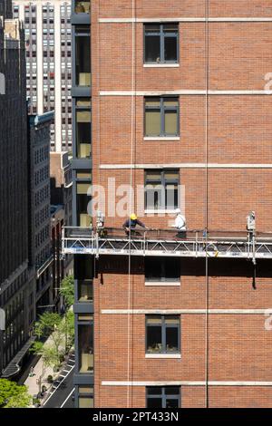 I lavoratori conducono un rimando di mattoni su una piattaforma sospesa in un edificio nel centro di Manhattan, 2023, New York City, Stati Uniti Foto Stock