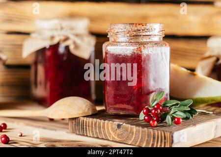 Vasetti di marmellata di lingoni e pere fatta in casa con carta artigianale su coperchi su superficie di legno accanto a bacche e pere fresche. Foto Stock