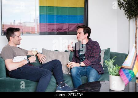 Giovane coppia lgtbi seduta sul divano chiacchierando e avendo un bicchiere di vino e rilassarsi buon tempo. Concetto: Stile di vita, orgoglio, amore Foto Stock