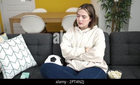 Giovane donna bionda che guarda la partita di calcio su smartphone con espressione nervosa per strada Foto Stock