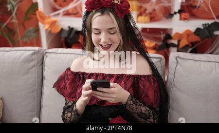 Giovane donna bionda che indossa il costume di katrina usando lo smartphone a casa Foto Stock