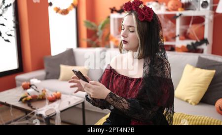 Giovane donna bionda che indossa il costume di katrina usando lo smartphone a casa Foto Stock