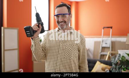 Uomo di mezza età che indossa occhiali di sicurezza che tengono il trapano a casa nuova Foto Stock