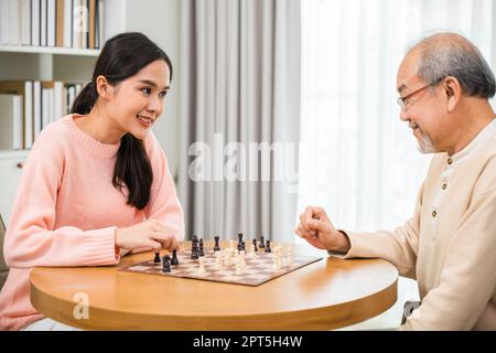 Bella giovane donna sorriso che ha divertimento seduto giocando a scacchi gioco con anziani anziani anziani anziani a casa, infermiere caregiver in casa di cura per il tempo libero, acti felice Foto Stock