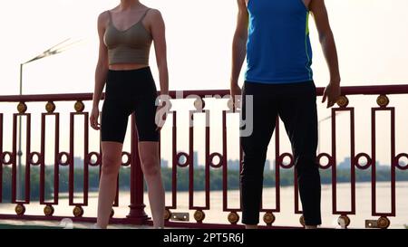 Coppia caucasica che si esercita sul ponte con bella vista facendo squats esercizio. Felice giovane uomo e donna che si allenano fuori. Allenamento all'aperto Foto Stock