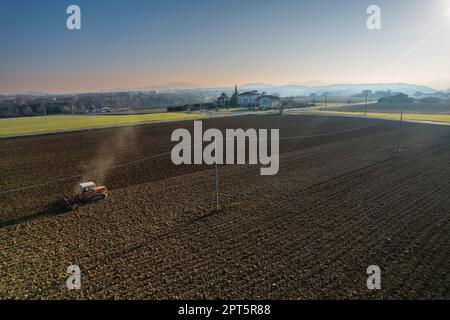 il contadino che guida un trattore cingolato trascina dietro una nuvola di polvere, arando, erpicando la rottura della crosta superficiale per facilitare la nascita e la semina di o Foto Stock