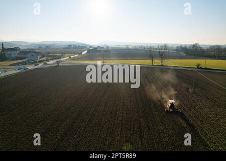 il contadino che guida un trattore cingolato trascina dietro una nuvola di polvere, arando, erpicando la rottura della crosta superficiale per facilitare la nascita e la semina di o Foto Stock