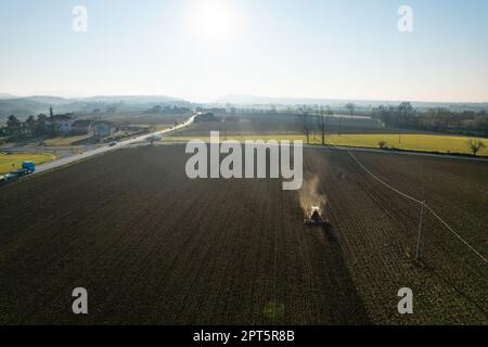 il contadino che guida un trattore cingolato trascina dietro una nuvola di polvere, arando, erpicando la rottura della crosta superficiale per facilitare la nascita e la semina di o Foto Stock