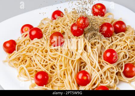 Il basilico essiccato viene cosparso di spaghetti con pomodori da cocktail, fotografia alimentare, piatto bianco, sfondo bianco Foto Stock