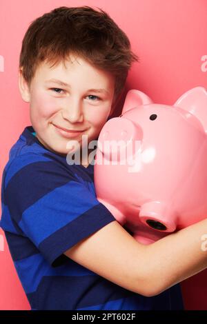 Abbracciando la sua ricchezza. Ritratto di un giovane ragazzo che tiene il suo piggybank Foto Stock