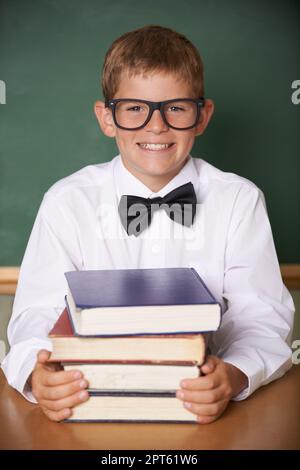 HES preparato per l'esame. Un giovane ragazzo felice che indossa occhiali e una cravatta sorridente alla macchina fotografica mentre si siede con un mucchio di libri Foto Stock