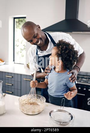 Adorabile ragazzino afroamericano con cottura afro in cucina a casa con suo padre . Allegro uomo nero guardando il suo bambino mentre mescolando ingre Foto Stock