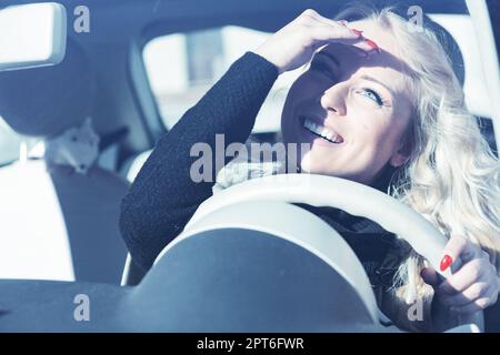 Bionda gal, ricci lunghi, trucco impeccabile, crociera città europea in un'auto alla moda. Lei è tutta sorride, colpisce le pose, e lascia che i suoi occhi brilli Foto Stock