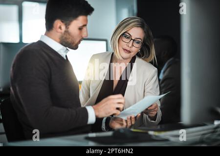 La comunicazione è fondamentale per il successo di molti progetti. due uomini d'affari discutono un documento mentre sono seduti alla scrivania. Foto Stock