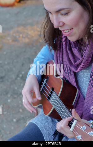 Vista dall'alto di una giovane bruna con capelli lunghi che gioca l'ukulele seduto nell'erba Foto Stock