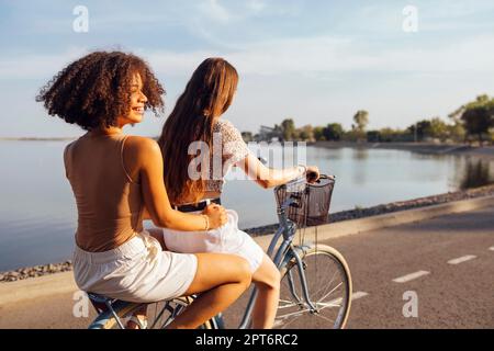 Adolescenti di diverse nazionalità e aspetto in bicicletta percorrono una strada cittadina. Le ragazze giovani e positive sorridono insieme. Stile di vita sano Foto Stock