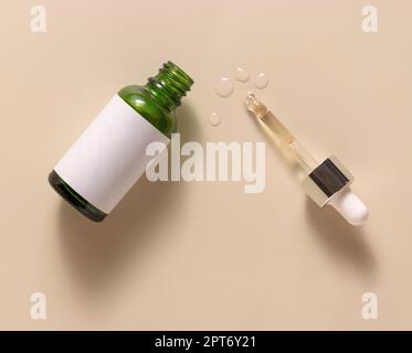 Flacone contagocce verde aperto con liquido in pipetta, vista dall'alto beige chiaro, mockup etichetta vuota. Prodotto, siero o essenza per la cura della pelle o della salute Foto Stock