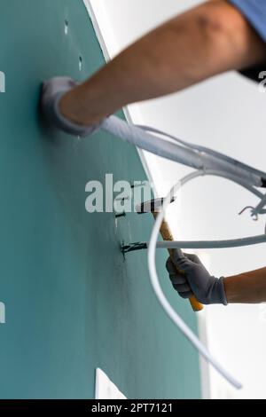 Primo piano del chiodo martellante nella parete. L'operatore maschio guida i perni nella parete prima di installare il condizionatore d'aria. Vista dal basso ad angolo delle mani che tengono hamme Foto Stock