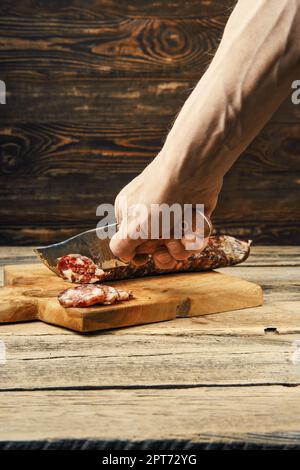 A mano con coltello tagliare salsiccia di maiale affumicata su fette di tagliere di legno Foto Stock