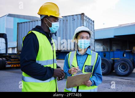 Covid, logistica e checklist dipendenti e maschera presso il cantiere, appunti e discutere il trasporto di merci. I dipendenti, uomini neri e donne asiatiche parlano Foto Stock