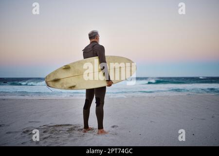 Surfista, surf e uomo anziano sulla spiaggia a onde di mare in durante il tramonto durante le vacanze estive alle Hawaii. L'atleta professionista si riposa dopo l'allenamento Foto Stock