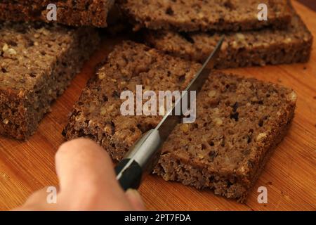 Una donna taglia un pezzo di pane integrale con un coltello. Sfocatura. Concetto di cibo sano. Foto Stock