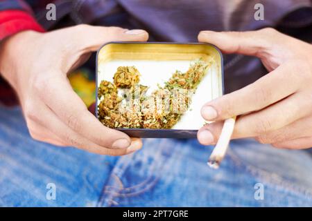 Sulla strada per l'inferno. Primo piano di una mano che tiene una scatola di teste di marijuana e un'articolazione Foto Stock