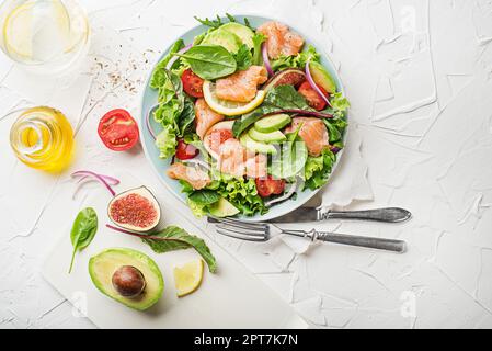 Insalata verde fresca con salmone affumicato, pomodori ciliegini, fichi e avocado su sfondo bianco Foto Stock