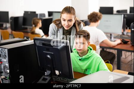 L'insegnante insieme agli studenti conduce una lezione sull'educazione informatica Foto Stock