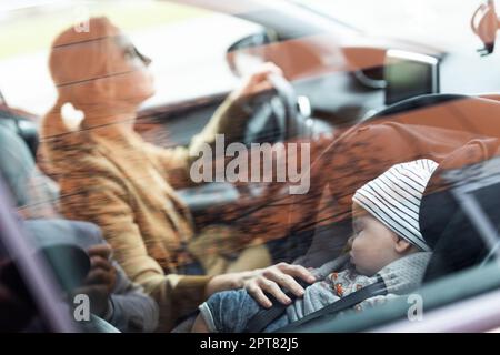 Madre che si concentra sulla guida di famiglia auto in esecuzione errands, mentre il suo bambino dorme in seggiolino auto per bambini dal suo sito Foto Stock