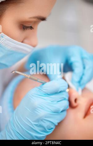 giovane donna durante una procedura meccanica di pulizia del viso in clinica di bellezza. Procedura di pulizia della pelle con utensile in acciaio dal nero Foto Stock