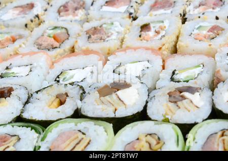 Primo piano di un sacco di sushi roll con diversi ripieni. Macrofo di cucina classica giapponese cotta. Immagine di sfondo Foto Stock